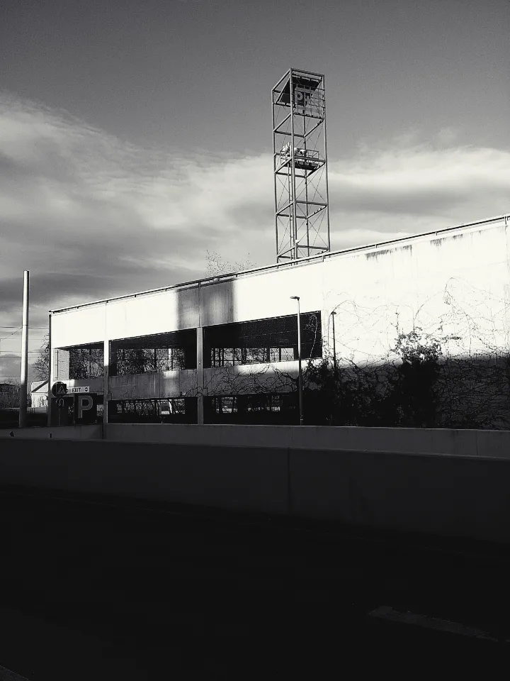 An industrial car park with a metal tower and some shrubbery.
