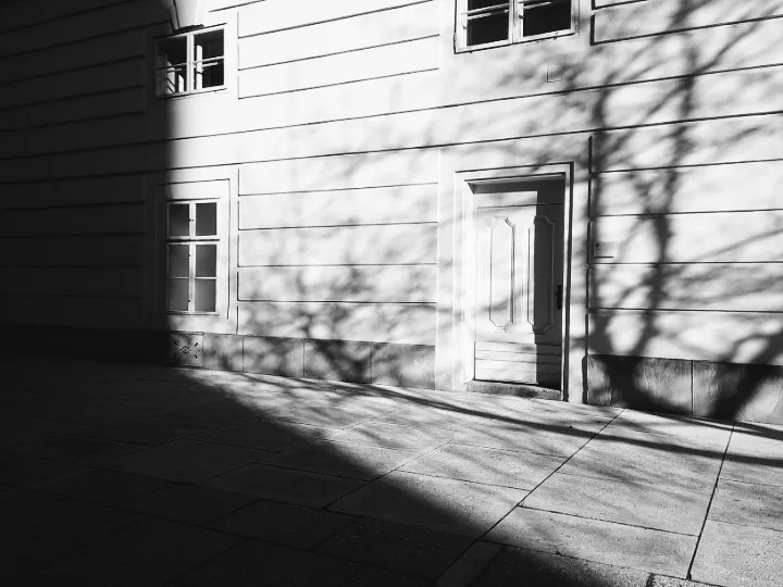 A street side facing the side of a building with a hard shadow cast from a building and part of a tree shadow against the wall