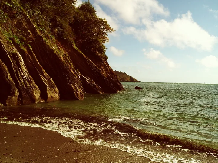 A beach scene with red sand and turquoise waters with rock cliff face descending into the sea